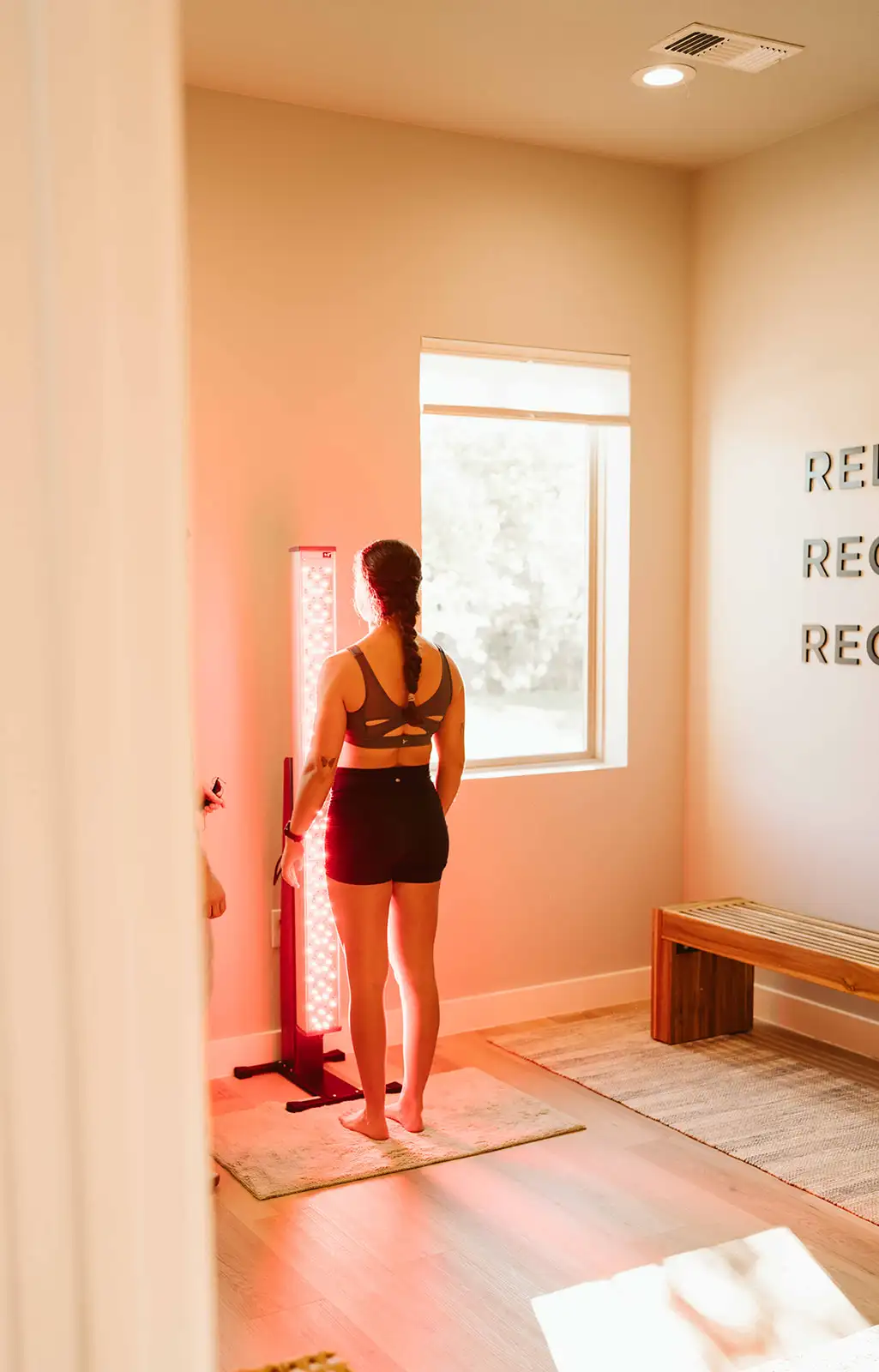 A woman standing in front of a red light therapy tower in the recovery room